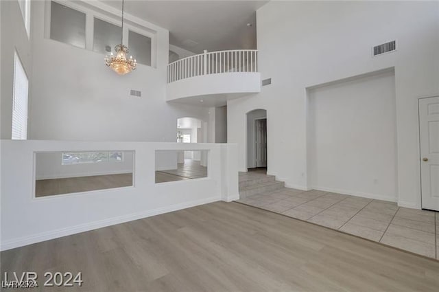 unfurnished living room featuring plenty of natural light, light wood-type flooring, and a high ceiling