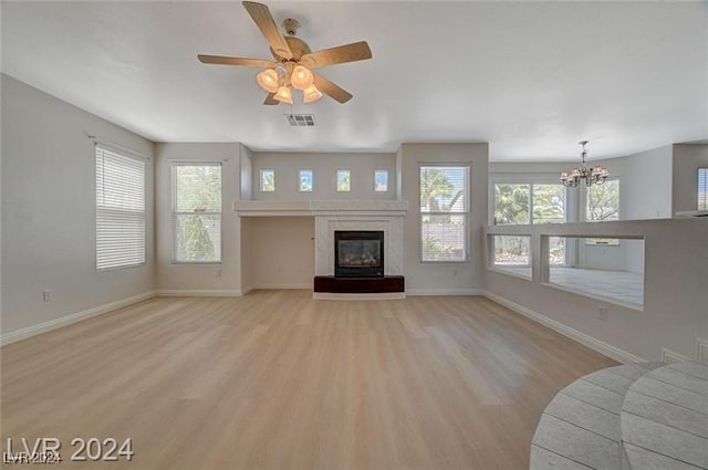 unfurnished living room with plenty of natural light, light wood-type flooring, and ceiling fan with notable chandelier