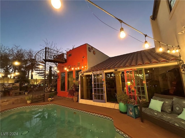 back house at dusk with an outdoor living space, a patio, and a balcony