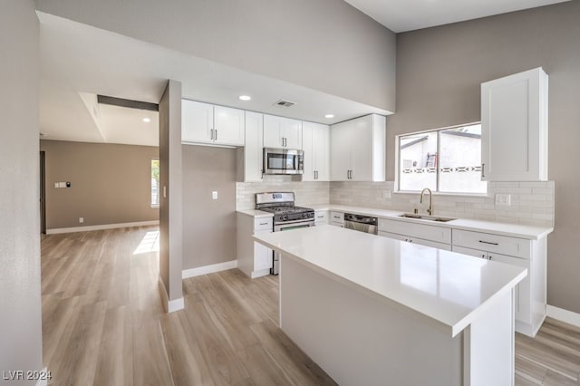 kitchen featuring appliances with stainless steel finishes, light wood-type flooring, sink, a center island, and white cabinetry