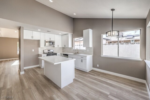 kitchen featuring light wood-type flooring, stainless steel appliances, sink, decorative light fixtures, and white cabinets