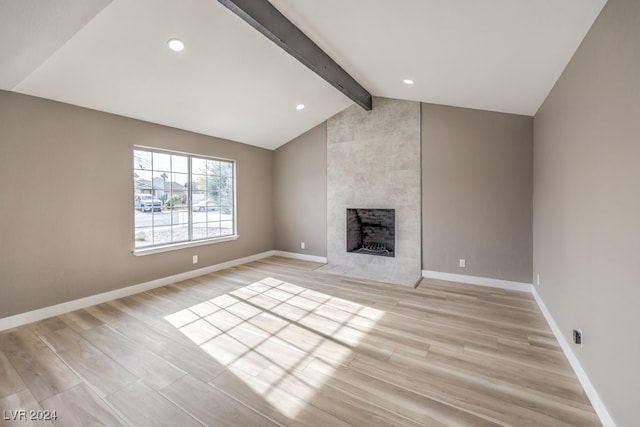 unfurnished living room featuring vaulted ceiling with beams, light wood-type flooring, and a tiled fireplace