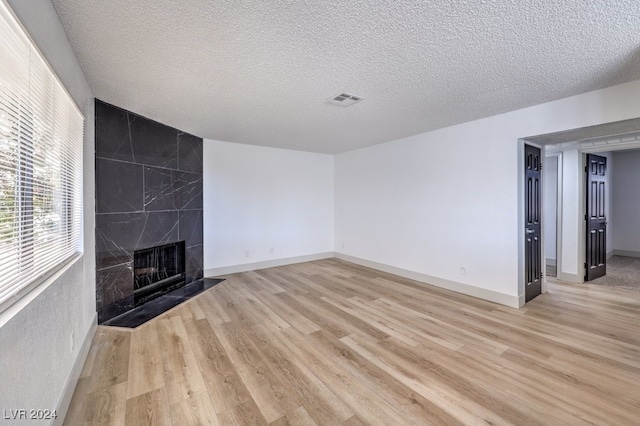 unfurnished living room featuring light hardwood / wood-style flooring, a high end fireplace, and a textured ceiling