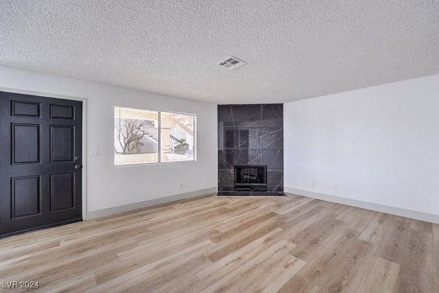 unfurnished living room featuring a high end fireplace, light hardwood / wood-style floors, and a textured ceiling