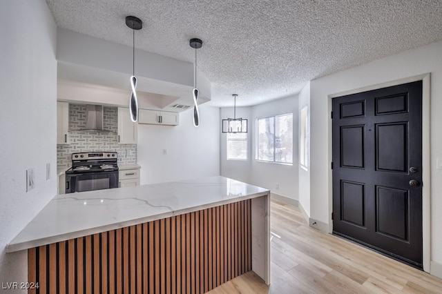 kitchen featuring light wood-type flooring, stainless steel range with electric stovetop, wall chimney range hood, white cabinetry, and hanging light fixtures