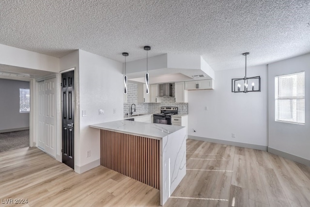 kitchen with white cabinets, stainless steel electric stove, wall chimney range hood, light hardwood / wood-style floors, and kitchen peninsula