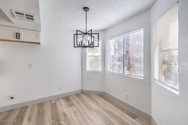 unfurnished dining area with a chandelier, a textured ceiling, and light hardwood / wood-style flooring