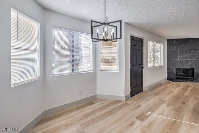 unfurnished dining area with a premium fireplace, a notable chandelier, a textured ceiling, and light wood-type flooring