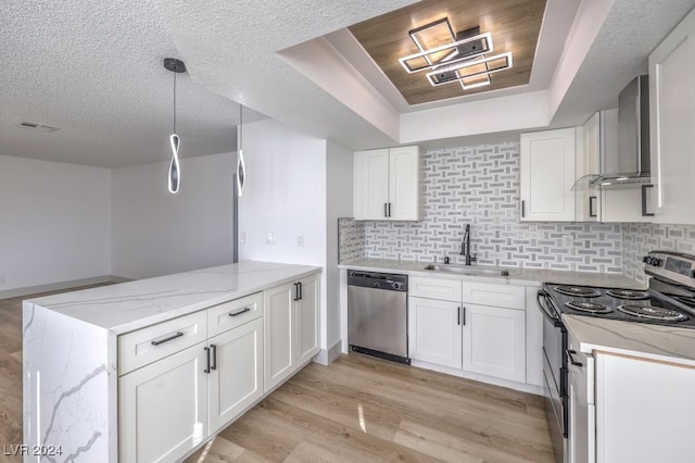 kitchen with sink, hanging light fixtures, stainless steel appliances, wall chimney range hood, and white cabinets