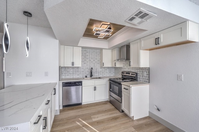 kitchen featuring white cabinetry, sink, wall chimney exhaust hood, hanging light fixtures, and stainless steel appliances