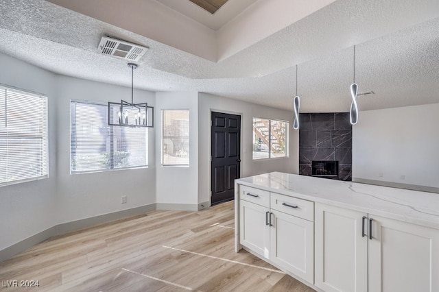 kitchen with a tile fireplace, light stone counters, a textured ceiling, white cabinets, and light wood-type flooring