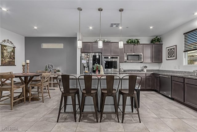 kitchen with light stone countertops, a breakfast bar, stainless steel appliances, decorative light fixtures, and a center island