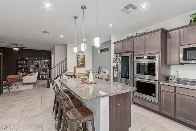 kitchen featuring light stone countertops, stainless steel appliances, light tile patterned floors, decorative light fixtures, and a center island