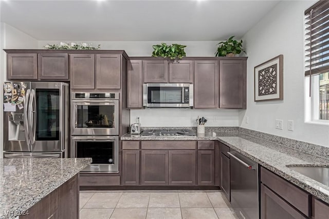 kitchen featuring light stone countertops, appliances with stainless steel finishes, dark brown cabinets, sink, and light tile patterned flooring