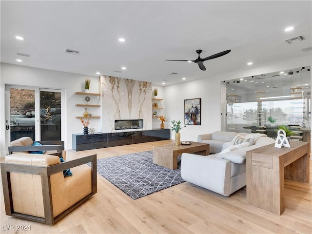 living room featuring a high end fireplace, light hardwood / wood-style floors, and ceiling fan