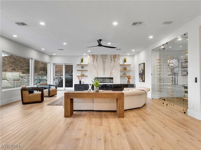 living room featuring light hardwood / wood-style floors, ceiling fan, and a premium fireplace