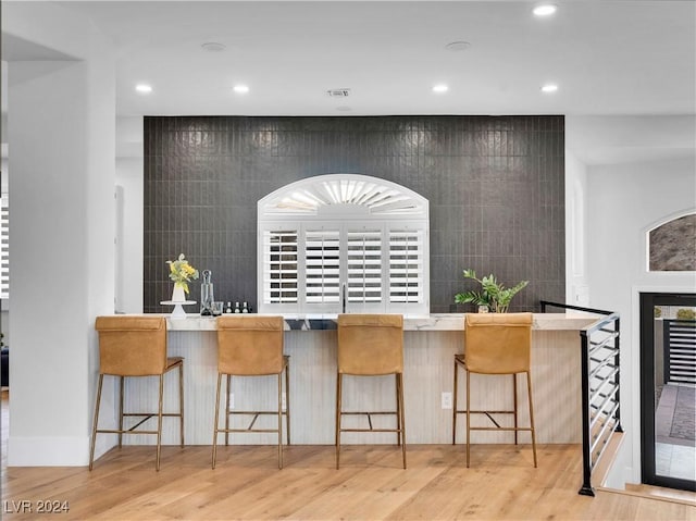 kitchen featuring a kitchen breakfast bar, light wood-type flooring, and tile walls