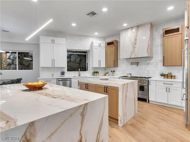 kitchen featuring white cabinets, stainless steel appliances, a kitchen island, and light stone counters