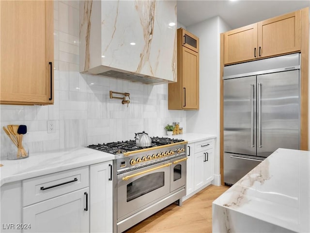 kitchen with light brown cabinets, premium appliances, backsplash, and range hood