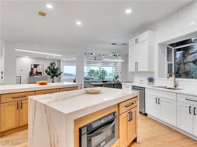 kitchen featuring a center island, white cabinets, sink, stainless steel dishwasher, and decorative light fixtures