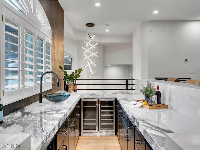 kitchen with light stone countertops, dark brown cabinetry, beverage cooler, sink, and decorative light fixtures