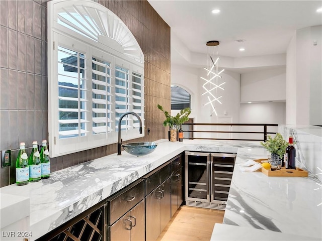 bar featuring sink, wine cooler, dark brown cabinets, light hardwood / wood-style floors, and light stone counters