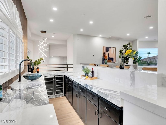 kitchen with light wood-type flooring, light stone counters, beverage cooler, and sink