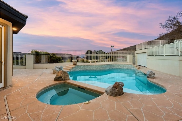 pool at dusk with a patio area and an in ground hot tub