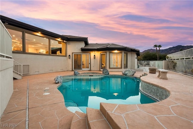 pool at dusk with a mountain view, a patio area, and an in ground hot tub