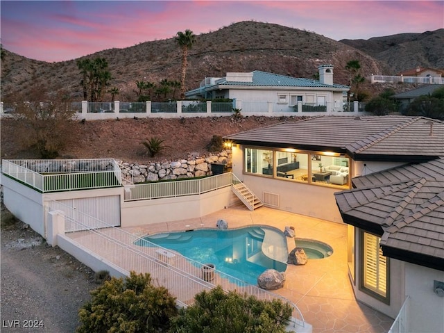 pool at dusk featuring a mountain view, a patio area, and an in ground hot tub