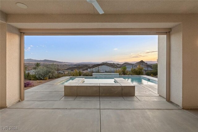 pool at dusk with a mountain view, ceiling fan, and a patio area