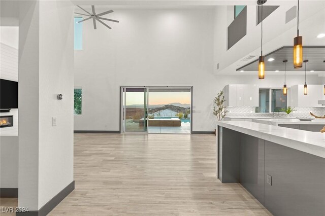 kitchen with pendant lighting, light hardwood / wood-style flooring, ceiling fan, tasteful backsplash, and a towering ceiling