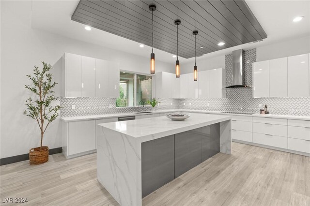 kitchen featuring a kitchen island, hanging light fixtures, white cabinets, and wall chimney range hood