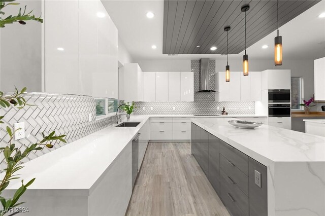 kitchen featuring a spacious island, pendant lighting, white cabinets, wall chimney range hood, and sink