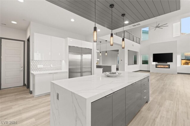 kitchen featuring built in fridge, a fireplace, white cabinetry, hanging light fixtures, and a kitchen island