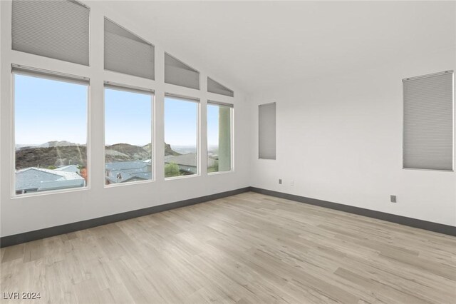 spare room with a mountain view, light hardwood / wood-style flooring, and lofted ceiling