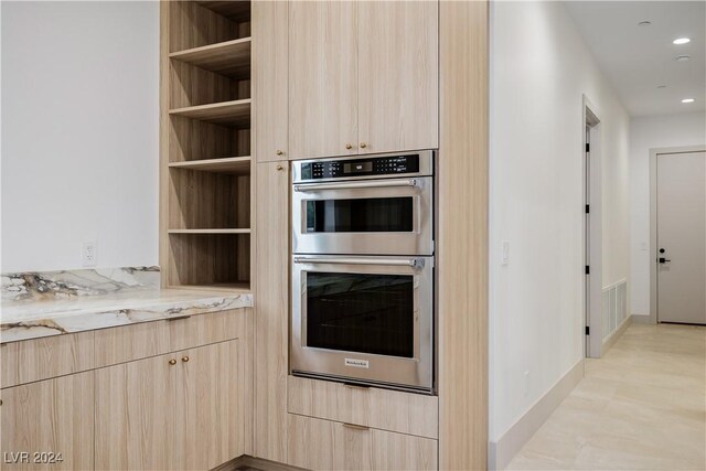 kitchen featuring light brown cabinets, light stone counters, double oven, and light hardwood / wood-style flooring