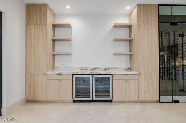 bar with light brown cabinetry, light stone counters, and beverage cooler