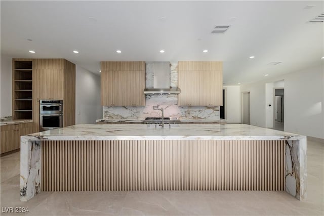 kitchen with backsplash, wall chimney exhaust hood, and a spacious island