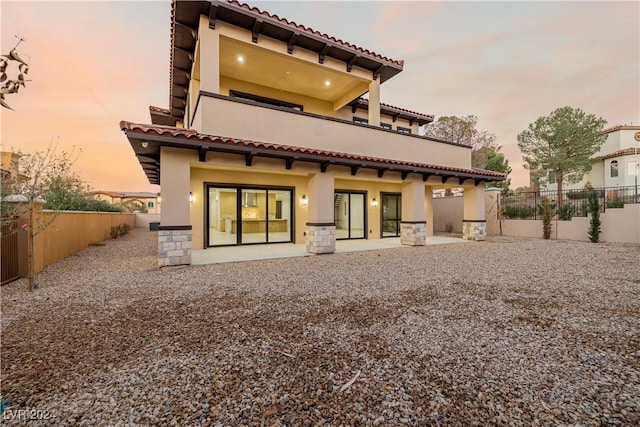 back house at dusk featuring a patio and a balcony