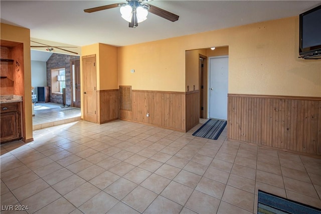 tiled empty room with ceiling fan, wooden walls, and vaulted ceiling