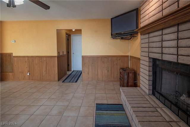 interior space with a fireplace, ceiling fan, wooden walls, and light tile patterned flooring