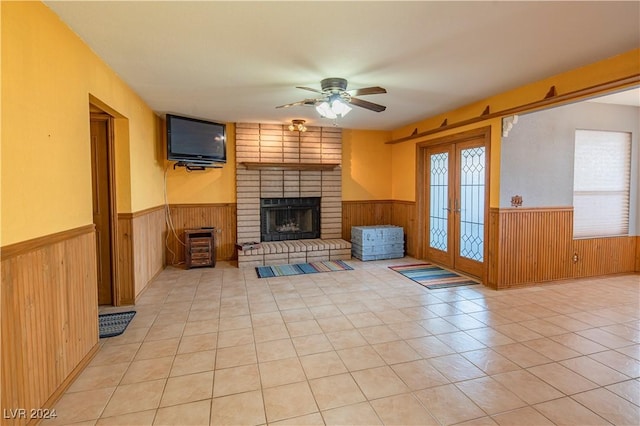 unfurnished living room featuring ceiling fan, french doors, wooden walls, and a brick fireplace