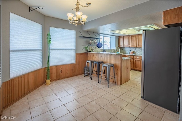 kitchen featuring a breakfast bar, wooden walls, a notable chandelier, kitchen peninsula, and stainless steel refrigerator