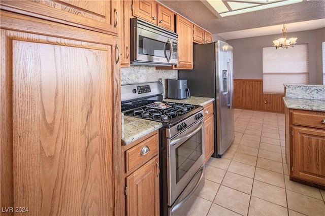 kitchen featuring light stone countertops, appliances with stainless steel finishes, a notable chandelier, and wood walls