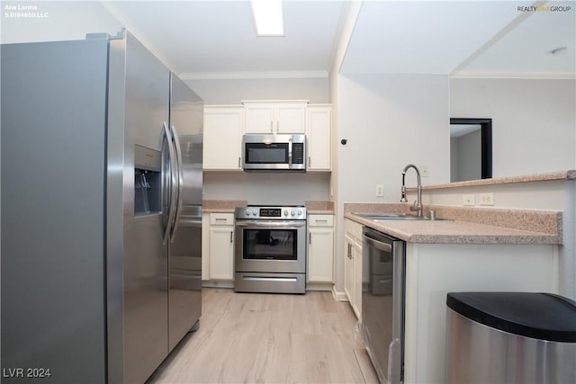 kitchen featuring light wood-style flooring, ornamental molding, a sink, white cabinetry, and appliances with stainless steel finishes