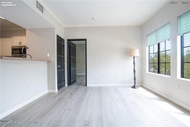 unfurnished living room with light wood-type flooring, crown molding, and baseboards