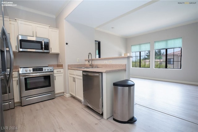 kitchen with a peninsula, a sink, stainless steel appliances, white cabinetry, and crown molding