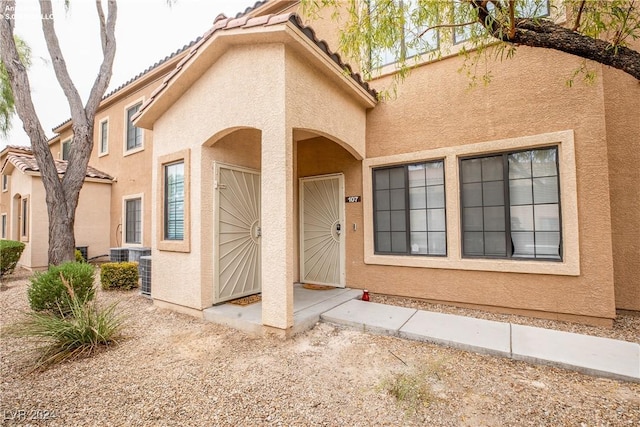 view of exterior entry with stucco siding, central AC unit, and a tiled roof