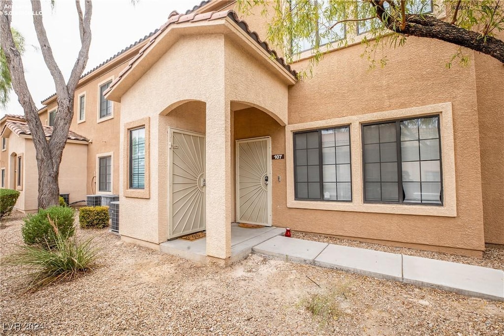 doorway to property with stucco siding, central AC, and a tiled roof